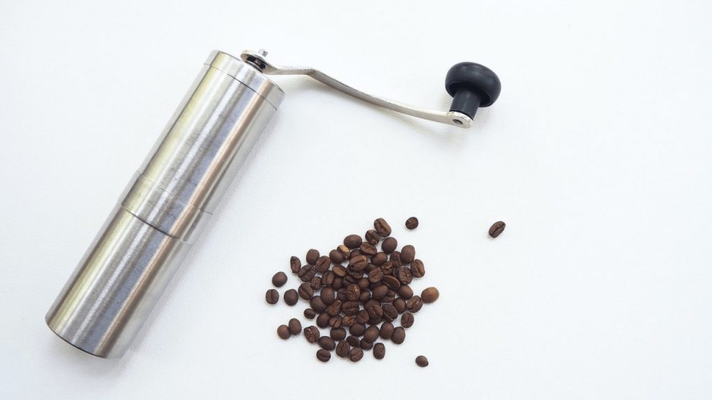 Steel manual coffee grinder and some coffee beans on a white table